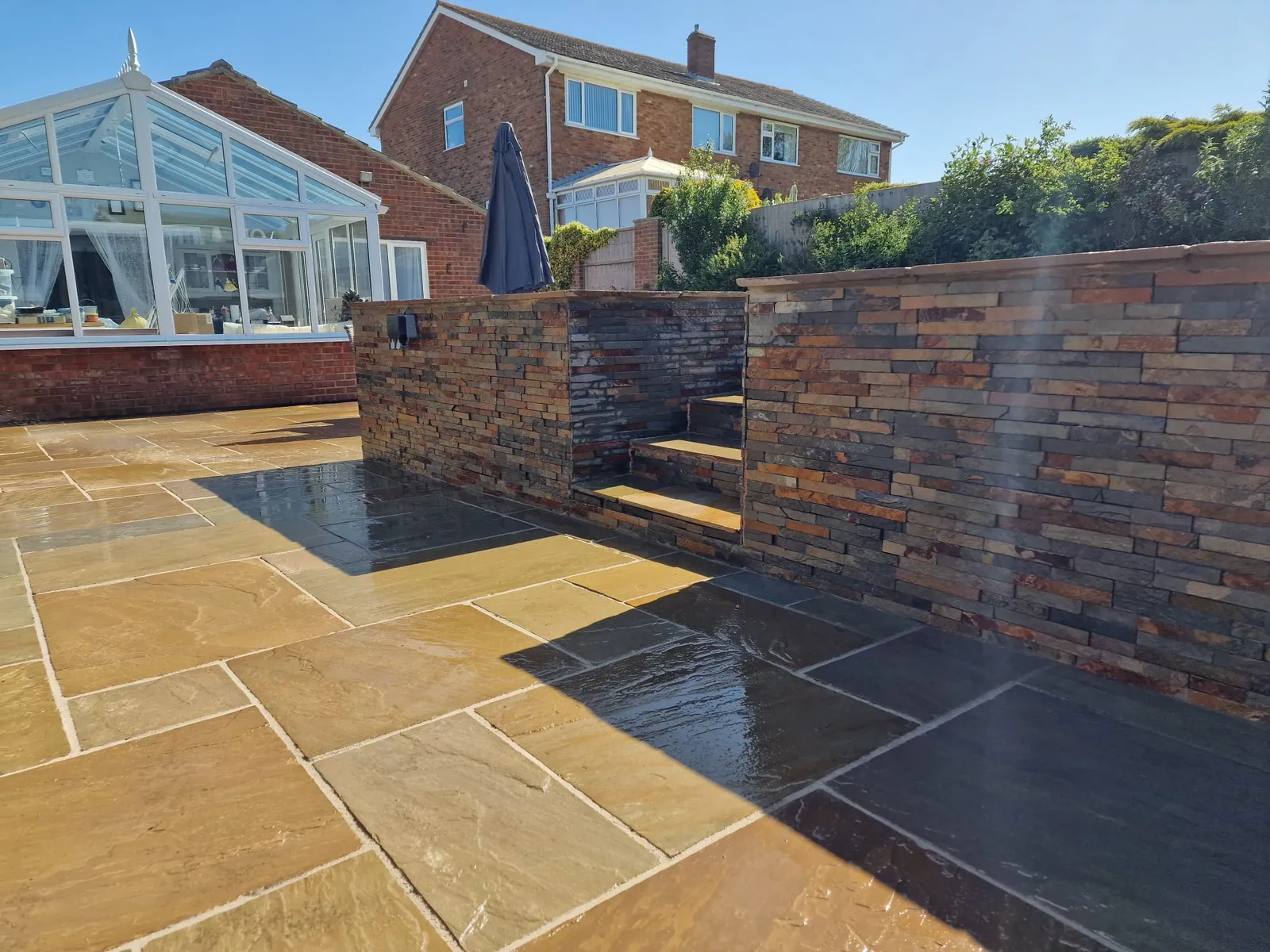 Natural stone patio and brick-faced raised walls behind a semi-detached house