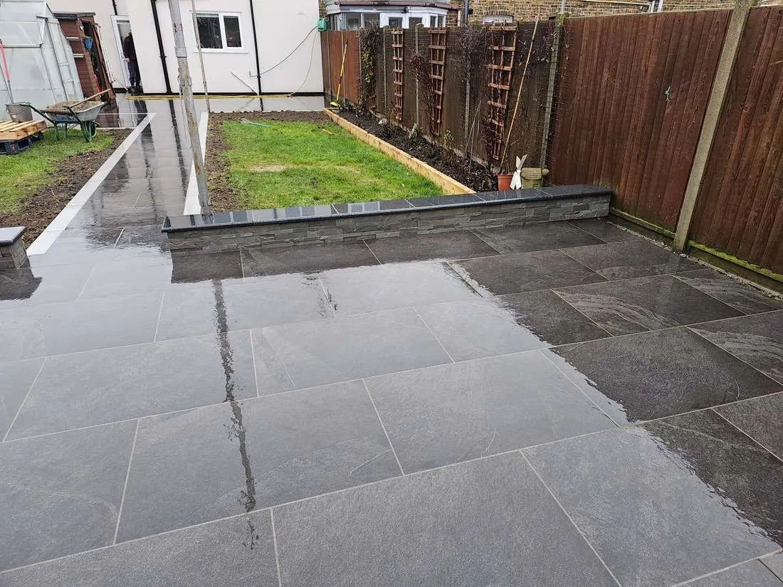 Dark porcelain patio with a low wall and lawn by DJG Groundworks