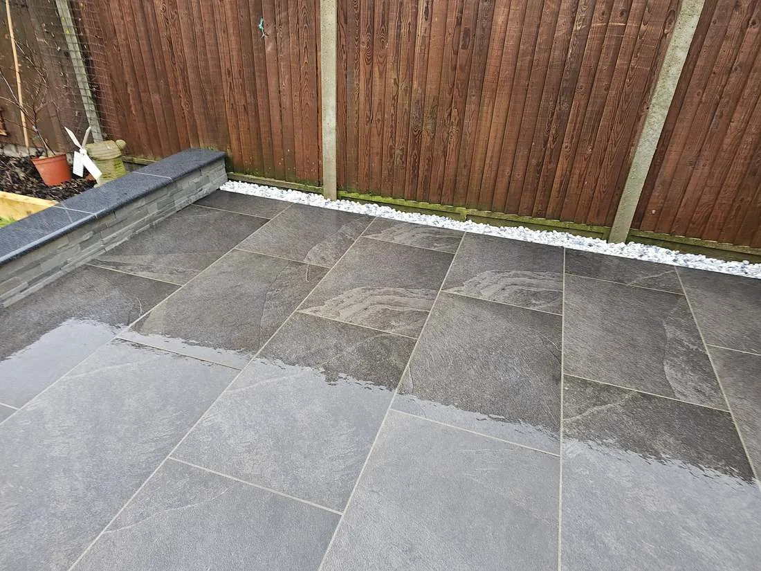 Dark porcelain patio with white pebble edging by DJG Groundworks