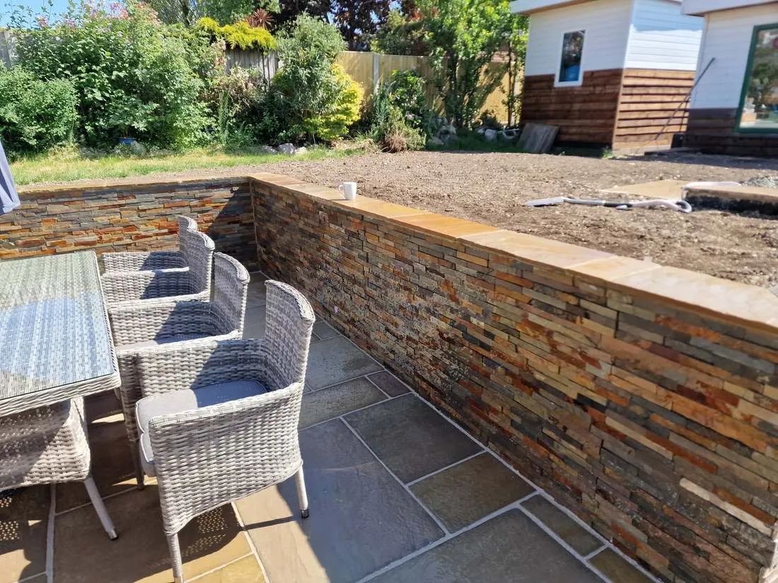 Sandstone patio below a slate-clad retaining wall by DJG Groundworks