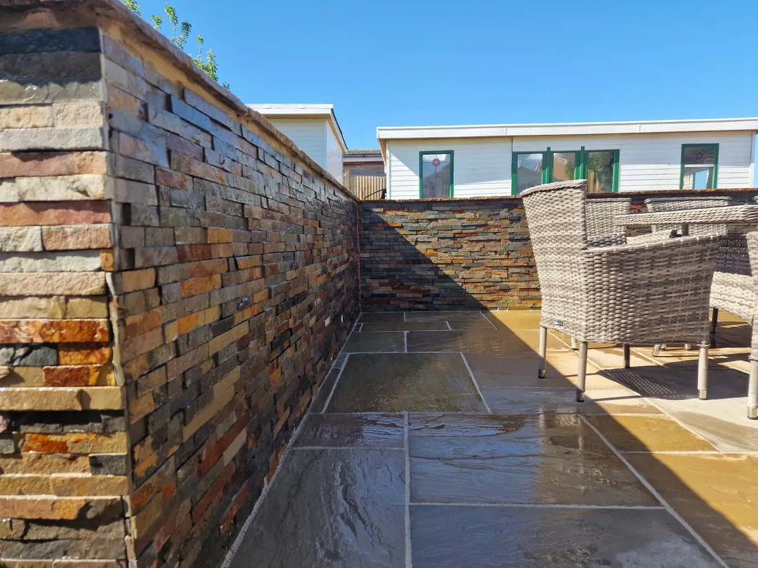Stone-clad retaining wall beside a patio by DJG Groundworks